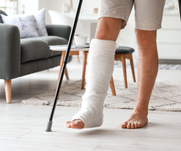 Personne avec un plâtre à la jambe et des béquilles, debout à l’intérieur. Cette image représente un symptôme courant de l’hypophosphatasie (HPP) : des fractures osseuses récurrentes, notamment dans les membres inférieurs.